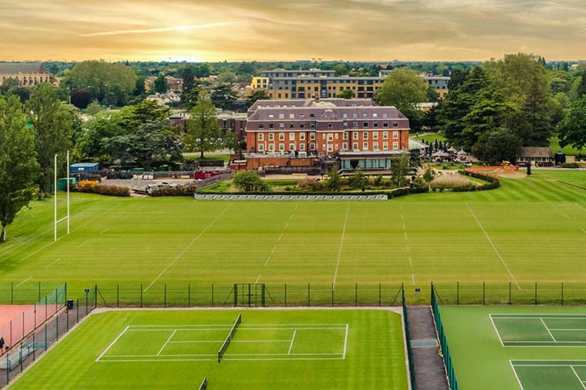Aerial view of tennis courts and The Lensbury hotel surrounded by greenery.