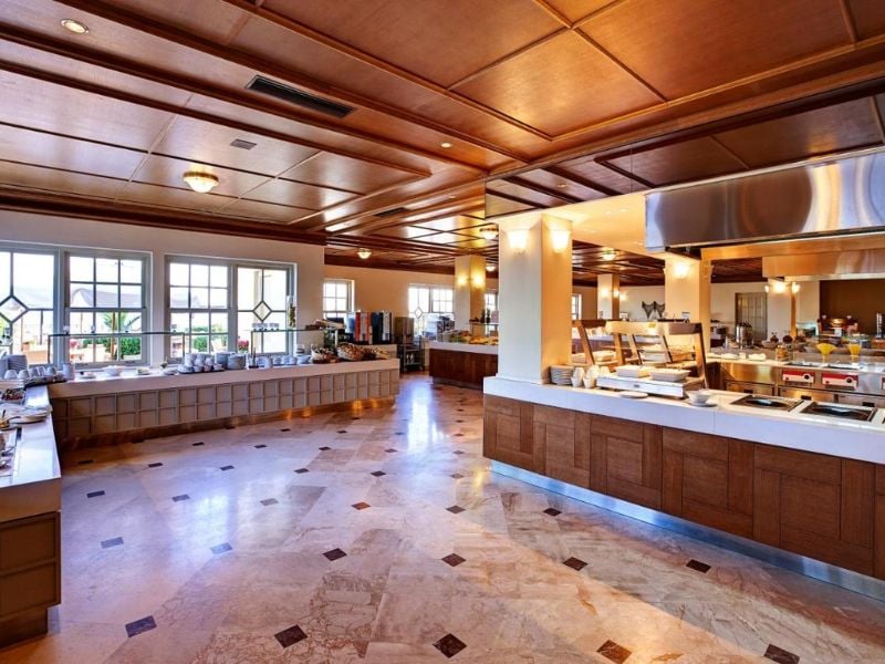 Kalimera Kriti Gallery buffet area with wooden décor, large windows, and various serving stations, filled with natural light.