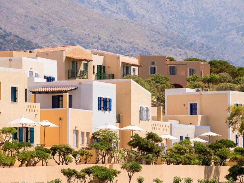 Mediterranean-style villas of Kalimera Kriti Gallery, featuring cream and pastel colours, surrounded by greenery and hills.