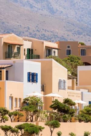 Mediterranean-style villas of Kalimera Kriti Gallery, featuring cream and pastel colours, surrounded by greenery and hills.