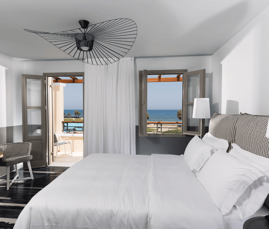 Deluxe sea view room at Kalimera Kriti Hotel with modern decor, double bed, and balcony overlooking the sea and pool.