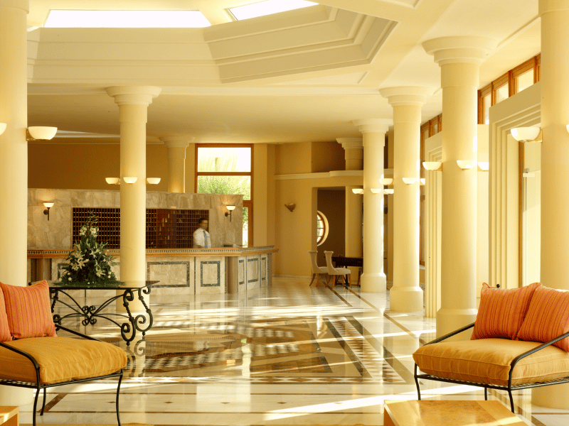 Lobby of Kalimera Kriti Hotel with marble flooring, elegant columns, arched windows, and comfortable seating.