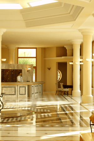 Lobby of Kalimera Kriti Hotel with marble flooring, elegant columns, arched windows, and comfortable seating.