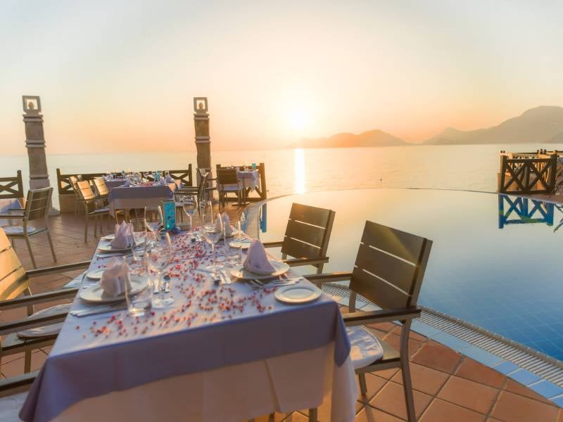 Dining table at Liberty Lykia Family Resort with sunset view over the sea and a poolside setting, showcasing elegant table settings.