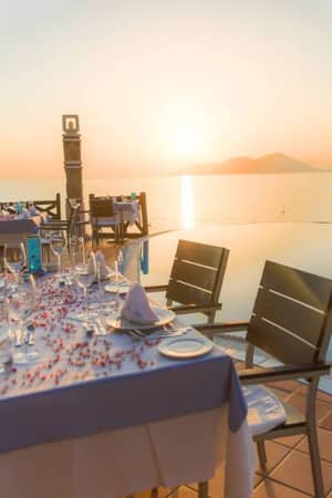Dining table at Liberty Lykia Family Resort with sunset view over the sea and a poolside setting, showcasing elegant table settings.