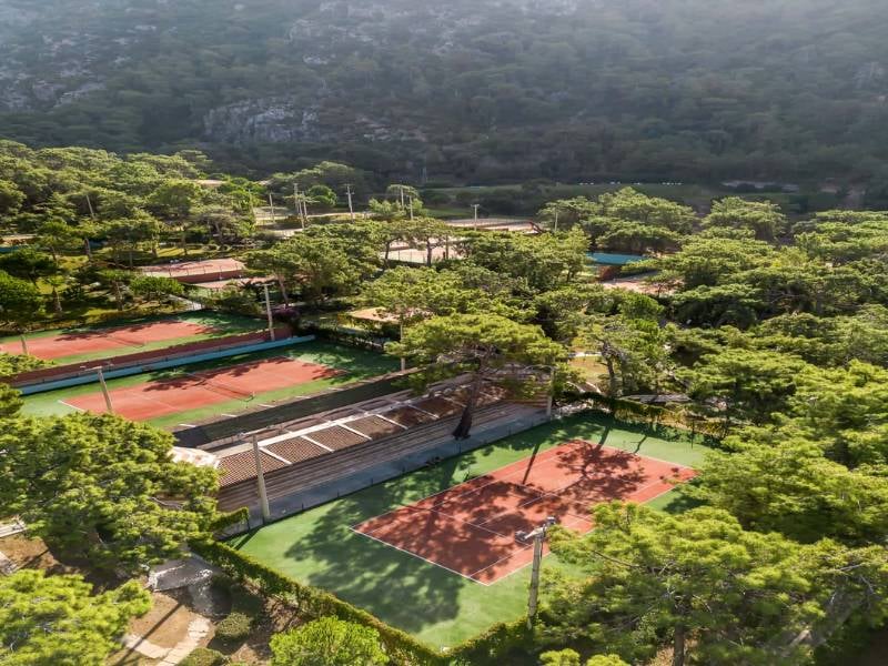 Drone view of Liberty Lykia Tennis Courts surrounded by trees and hills, showcasing a serene forest location.