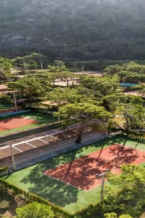 Drone view of Liberty Lykia Tennis Courts surrounded by trees and hills, showcasing a serene forest location.