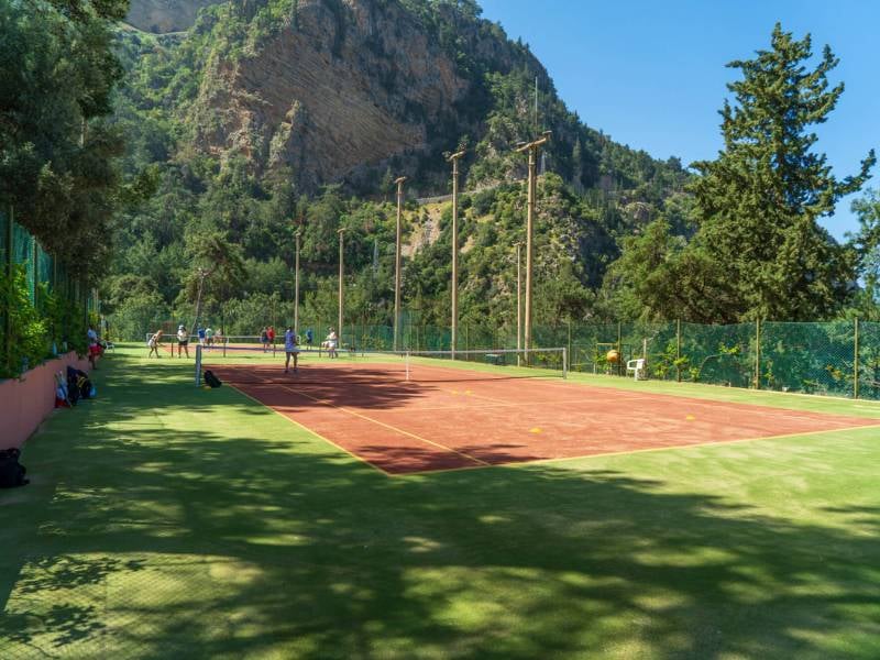 Tennis courts at Liberty Lykia surrounded by greenery and mountains, with players actively competing.