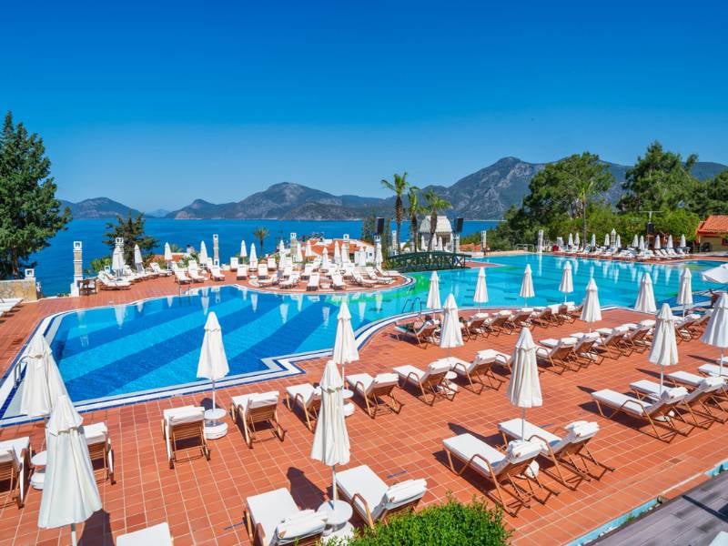 Liberty Lykia resort swimming pool with sun loungers and parasols, overlooking the sea and mountains.