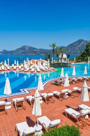 Liberty Lykia resort swimming pool with sun loungers and parasols, overlooking the sea and mountains.