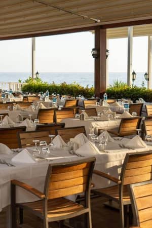 Open-air restaurant at Liberty Lykia Resort with tables set with white tablecloths and wooden chairs, overlooking the sea.
