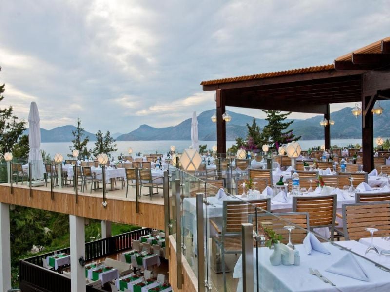 Liberty Lykia rooftop restaurant with sea and mountain views, featuring white tablecloths and wooden seating under a pergola.