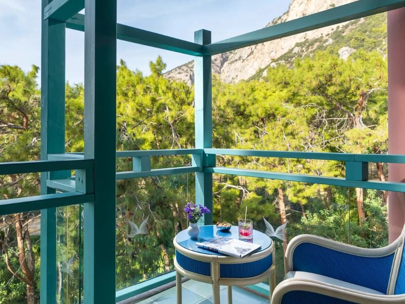 Balcony at Liberty Lykia featuring a table with drinks, a plant, and views of green trees and mountains.