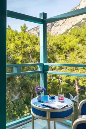 Balcony at Liberty Lykia featuring a table with drinks, a plant, and views of green trees and mountains.