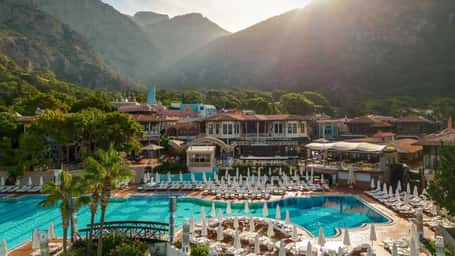 Liberty Lykia Village resort with a large outdoor pool, surrounded by sun loungers and lush mountain scenery in the background.