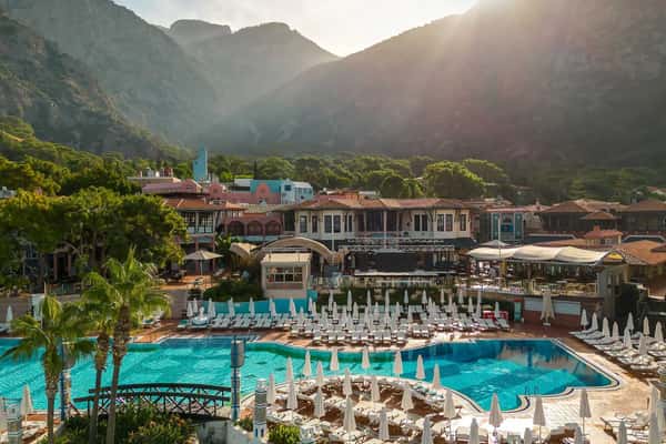 Liberty Lykia Village resort with a large outdoor pool, surrounded by sun loungers and lush mountain scenery in the background.