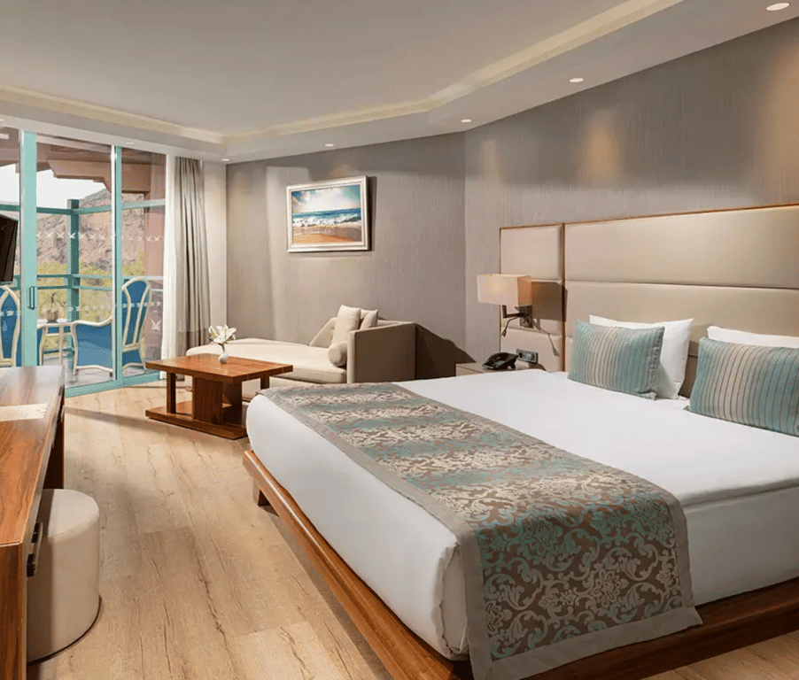 Interior of the Liberty Sentido Deluxe Standard Land Side room with a king-size bed, decorative pillows, a sofa, and a balcony view.