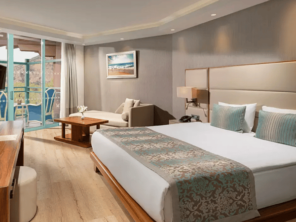 Interior of the Liberty Sentido Deluxe Standard Land Side room with a king-size bed, decorative pillows, a sofa, and a balcony view.