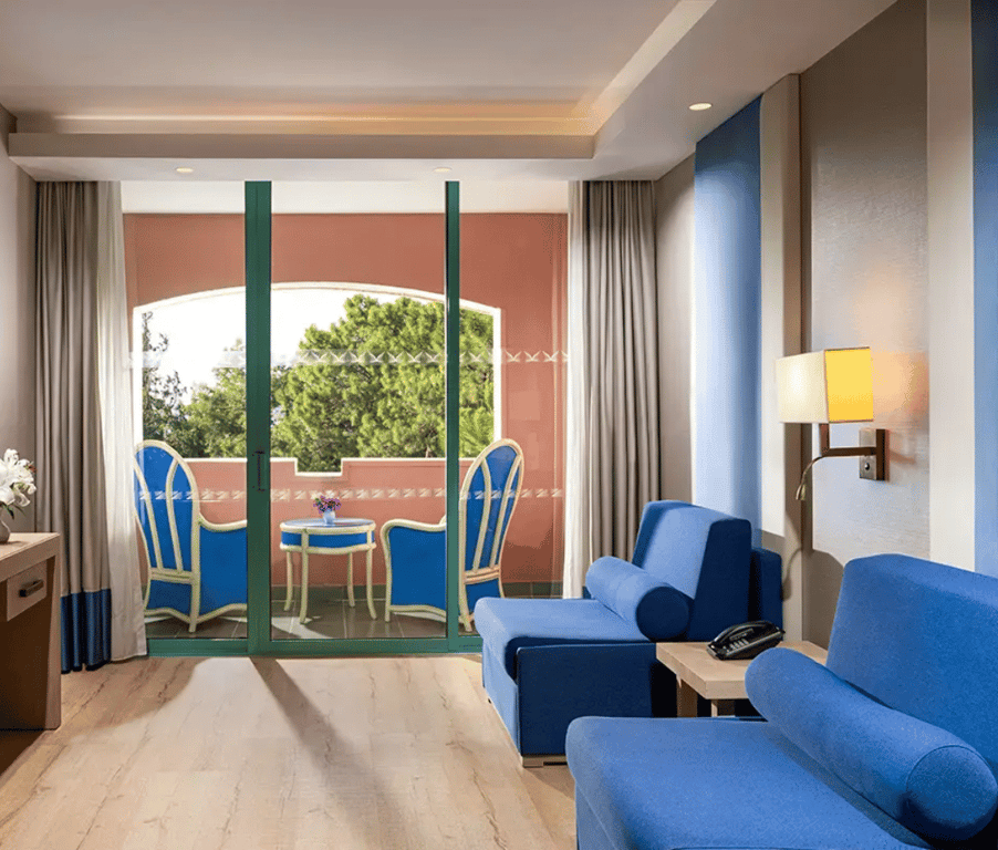 Luxurious Liberty Sentido Deluxe Suite interior with blue sofas, a private balcony, and verdant views through sliding glass doors.
