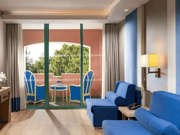 Luxurious Liberty Sentido Deluxe Suite interior with blue sofas, a private balcony, and verdant views through sliding glass doors.