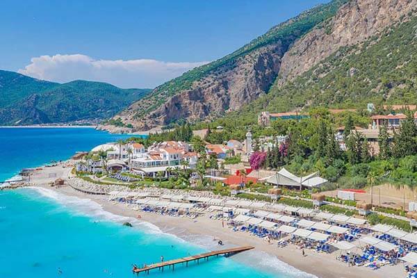 Seaside resort with beach umbrellas, wooden pier, and mountains in the background, part of Liberty Sentido Events location.