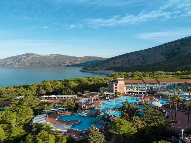 Aerial view of Liberty Sentido Gallery resort, highlighting the pool area, surrounding greenery, and bay with mountains in the background.