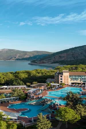 Aerial view of Liberty Sentido Gallery resort, highlighting the pool area, surrounding greenery, and bay with mountains in the background.
