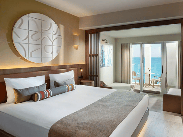 Luxurious hotel room at Liberty Village with a large bed, modern decor, and a balcony overlooking the sea.