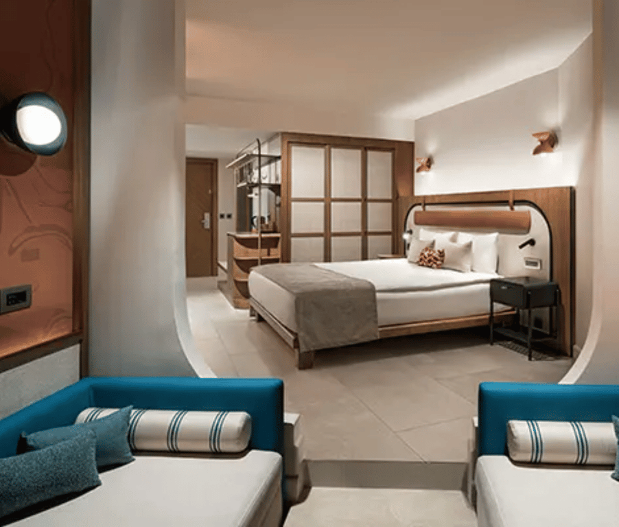 Modern hotel room at Liberty Village Deluxe with king-sized bed, wooden furnishings, blue seating, and partial sea view.