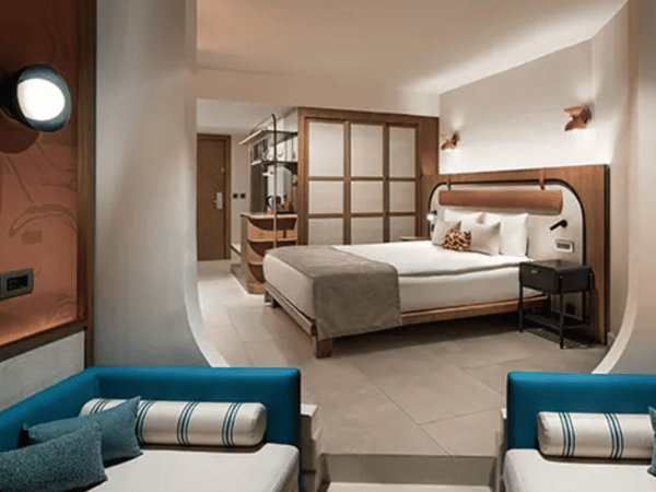 Modern hotel room at Liberty Village Deluxe with king-sized bed, wooden furnishings, blue seating, and partial sea view.