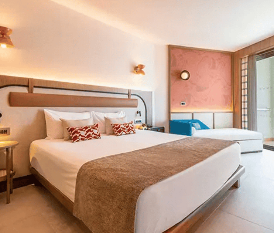 Hotel room at Liberty Village Deluxe with a large double bed, white linens, patterned cushions, and modern decor including a balcony door and wooden accents.
