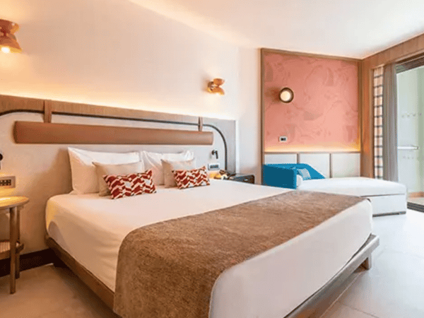 Hotel room at Liberty Village Deluxe with a large double bed, white linens, patterned cushions, and modern decor including a balcony door and wooden accents.