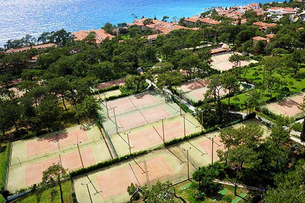 Aerial view of Liberty Village showing multiple tennis courts amidst greenery and close to a blue sea.
