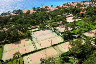 Aerial view of Liberty Village showing multiple tennis courts amidst greenery and close to a blue sea.