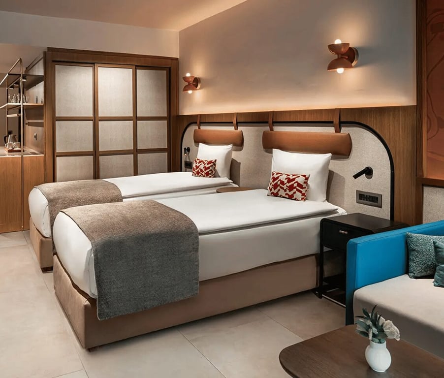 Liberty Village FTH Deluxe Family Room showcasing two single beds, decor featuring wood panels, a blue sofa, and a view of the sea from the side.