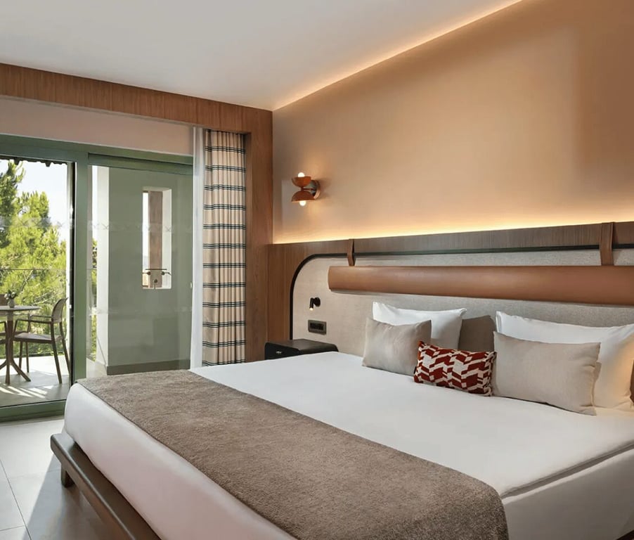 Hotel room at Liberty Village with a large bed, balcony, and side sea view, decorated with modern furniture and warm tones.