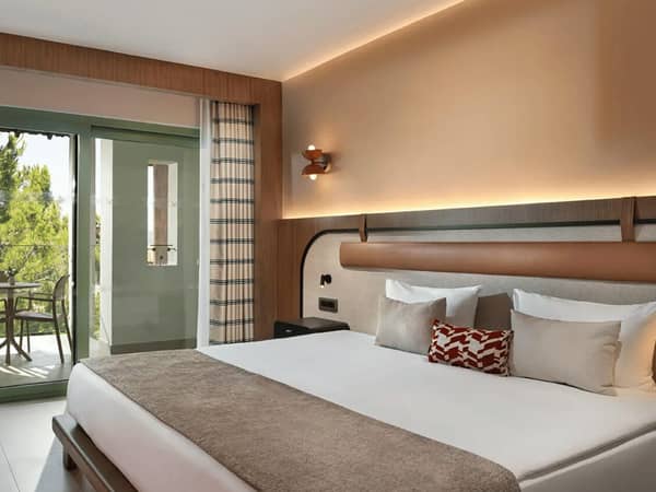 Hotel room at Liberty Village with a large bed, balcony, and side sea view, decorated with modern furniture and warm tones.