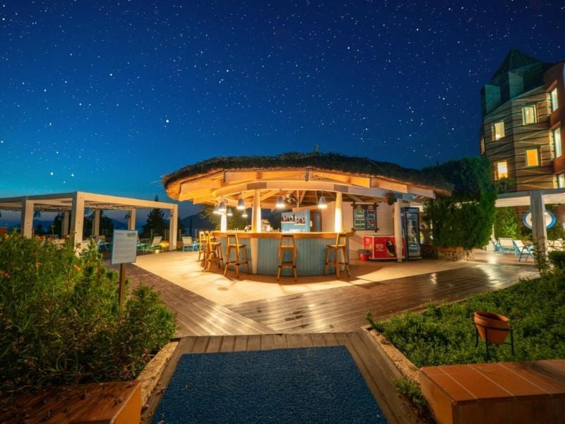 Night bar at Liberty Village Gallery with a round thatched roof, wooden stools, surrounded by greenery, and a star-filled sky.
