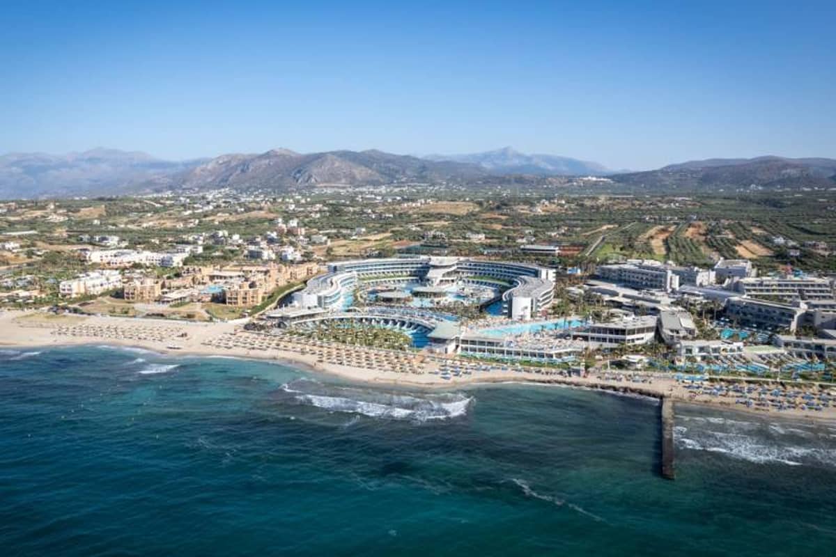 Aerial view of Lyttos Beach Resort in Crete, Greece, showcasing pools, beach, and mountainous backdrop.