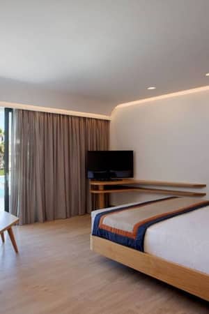 Hotel room at Lyttos Gallery with a bed, sofa, and TV, overlooking palm trees through a glass door.