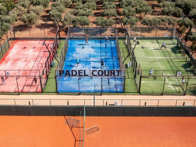 Aerial view of Lyttos Mare's padel courts with players, featuring red, blue, and green courts surrounded by an olive grove.