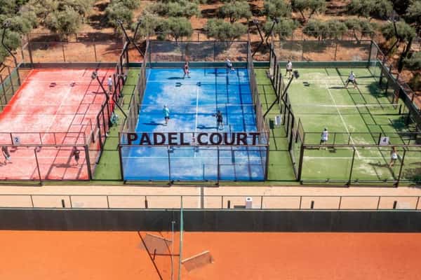 Aerial view of Lyttos Mare's padel courts with players, featuring red, blue, and green courts surrounded by an olive grove.