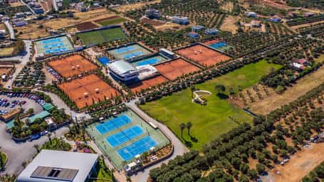 Aerial view of Lyttos Mare resort in Crete with padel and tennis courts surrounded by greenery and accommodations.
