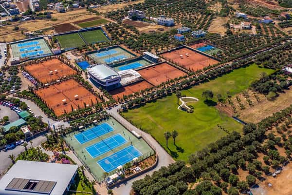 Aerial view of Lyttos Mare resort in Crete with padel and tennis courts surrounded by greenery and accommodations.