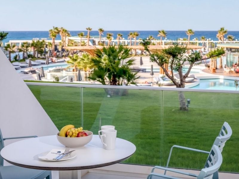 Lyttos Mare Resort balcony view with table and chairs, overlooking the pool, gardens, and sea.