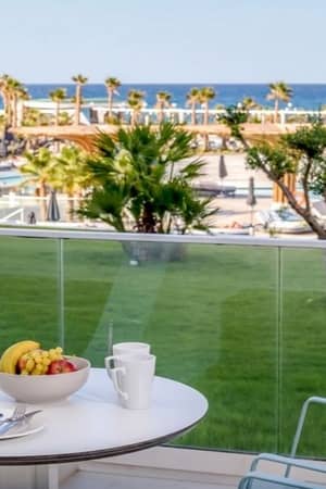 Lyttos Mare Resort balcony view with table and chairs, overlooking the pool, gardens, and sea.
