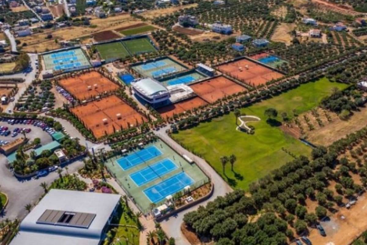 Aerial view of the Lyttos Mare tennis complex with multiple clay and hard tennis courts, olive groves, and a central building.