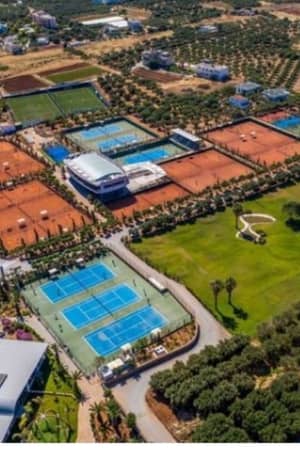 Aerial view of Lyttos Mare's tennis courts, featuring several clay and hard surfaces in a green setting.