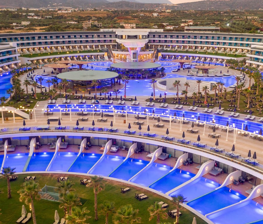 Overhead view of Lyttos Mare Resort at night, with a large central pool and private plunge pools, illuminated beautifully.