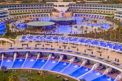 Overhead view of Lyttos Mare Resort at night, with a large central pool and private plunge pools, illuminated beautifully.